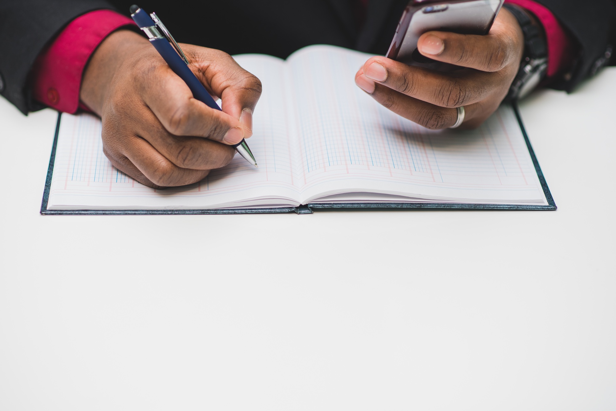 African American man doing accounting with smartphone calculator and ledger book